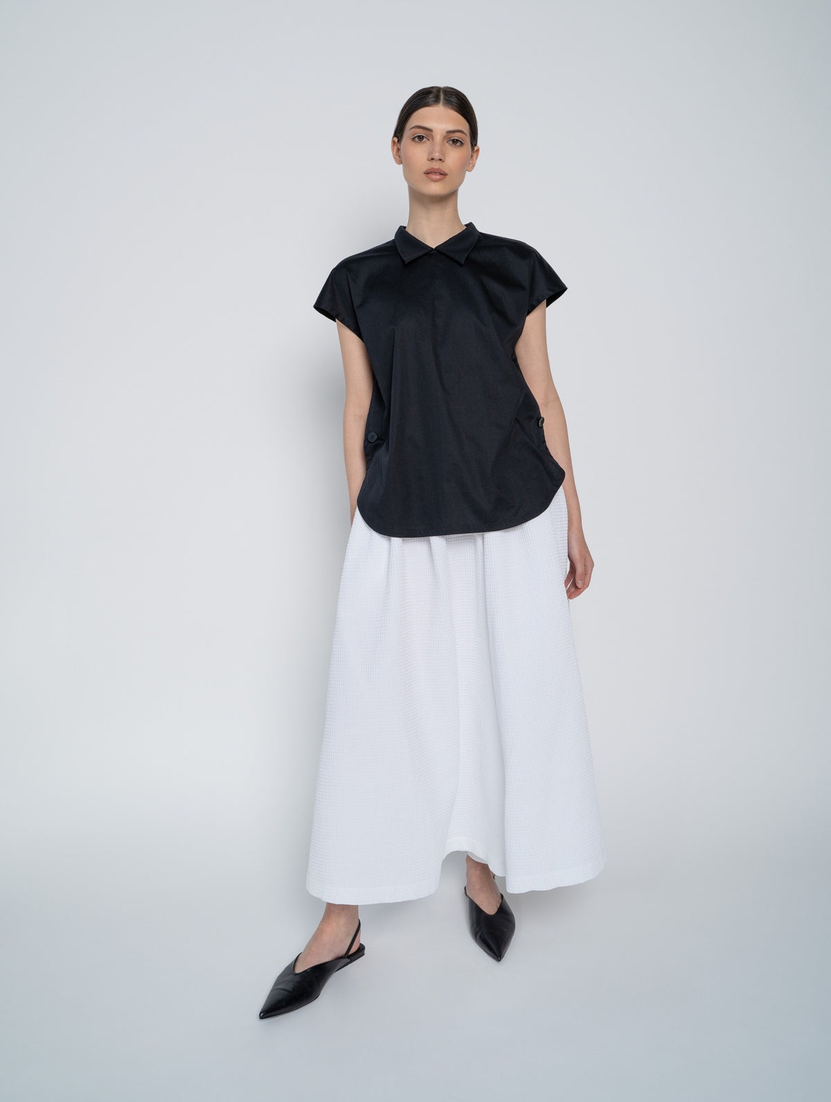 Schwarze, ärmellose Bluse mit Flügelkragen und Knöpfen auf der Vorderseite neben der Seitennaht.