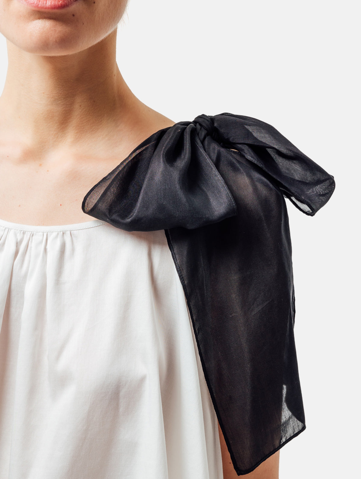 Weit geschnittenes Tanktop aus weißer Baumwolle mit schwarzem Schleifendetail und seperaten Gürtel aus schwarzer Baumwolle. Versteckte Seitentaschen in den Seitennähten. Dieses Produkt ist Teil unserer Reborn Linie.