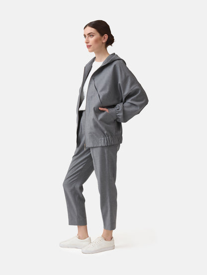Locker geschnittene Blousonjacke mit Kapuze und Reißverschluss, sowie dreiecksförmiger Kängurutasche im Vorderteil und elastischem Bündchen am Saumende. Dieses Modell ist Teil unserer REBORN-Linie und steht für unsere "Zero-Waste-Politik", da mit Stoff aus Altbestand gefertigt.