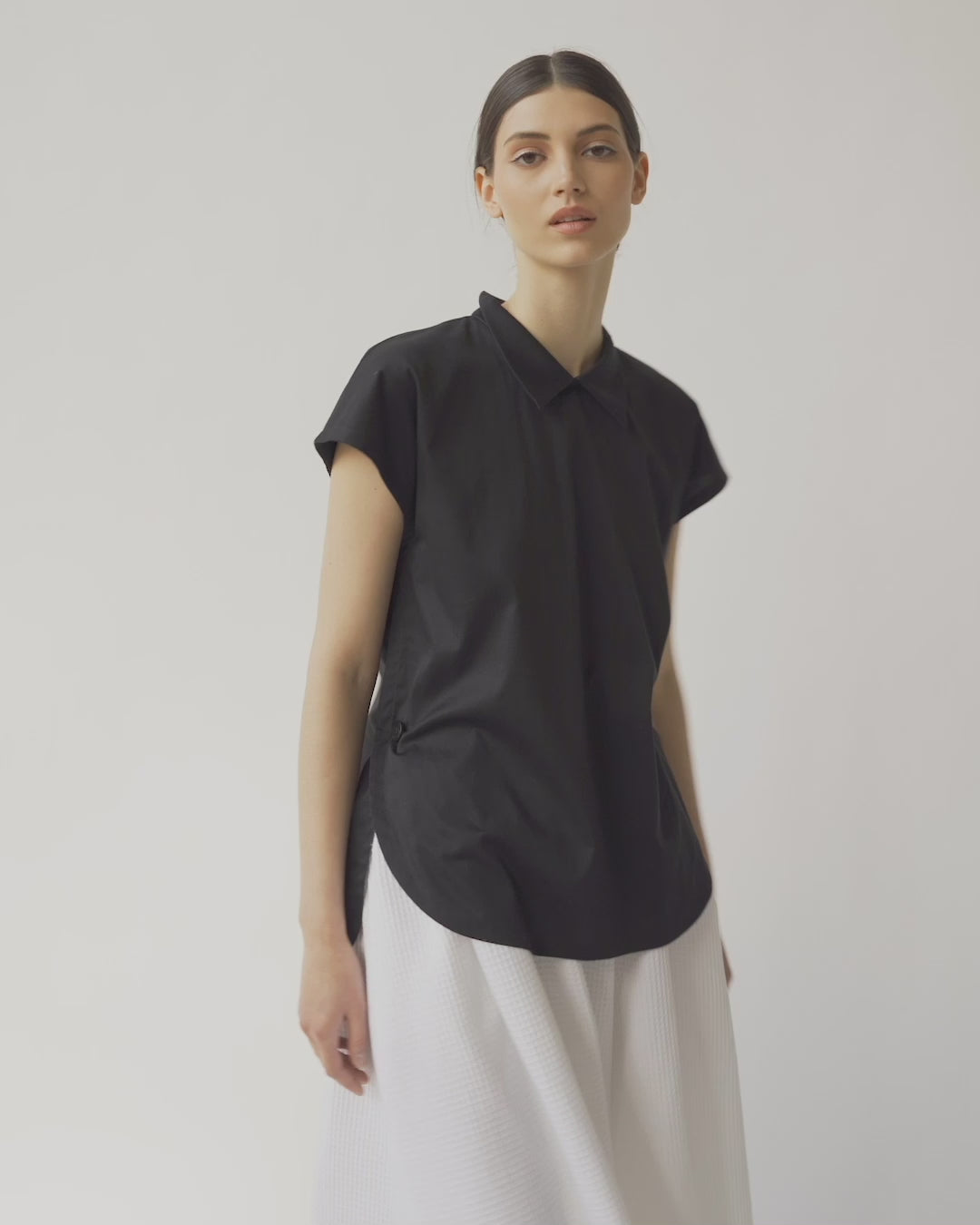 Schwarze, ärmellose Bluse mit Flügelkragen und Knöpfen auf der Vorderseite neben der Seitennaht